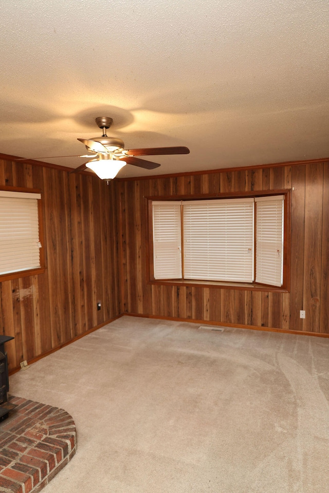 unfurnished living room with wood walls, light colored carpet, a wood stove, and ceiling fan