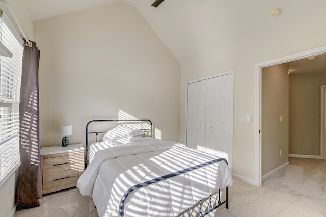 bedroom with ceiling fan, light colored carpet, high vaulted ceiling, and a closet