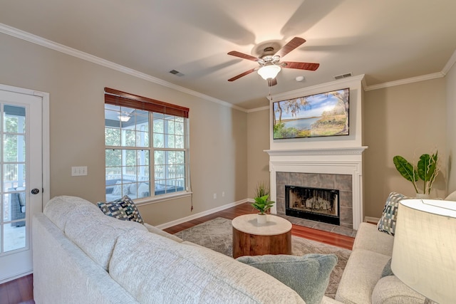 living room featuring hardwood / wood-style flooring, ceiling fan, ornamental molding, and a tile fireplace