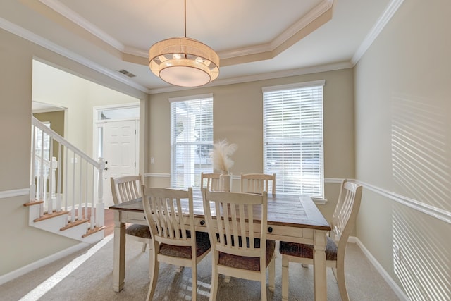 carpeted dining room with a healthy amount of sunlight, ornamental molding, and a tray ceiling