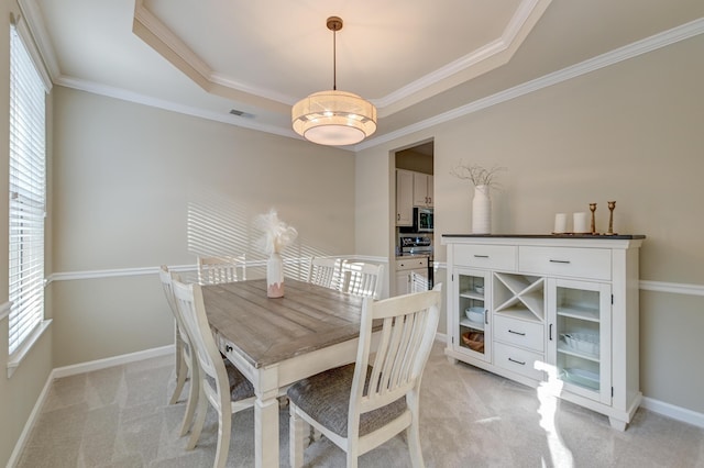 carpeted dining space with a raised ceiling and ornamental molding