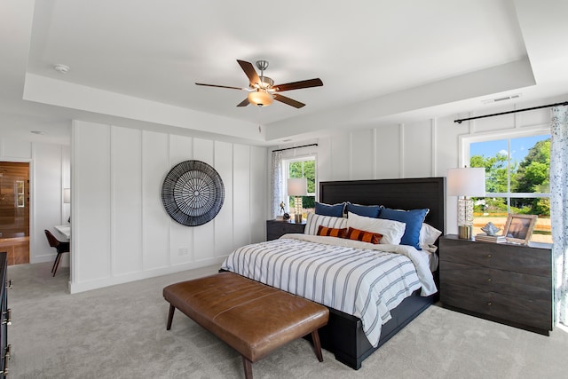 carpeted bedroom featuring ensuite bath, a raised ceiling, and ceiling fan