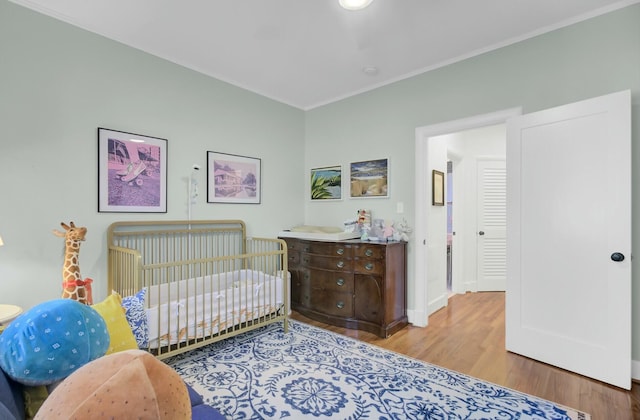 bedroom featuring crown molding, light hardwood / wood-style floors, and a nursery area