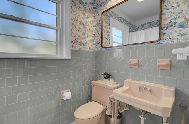 bathroom with toilet, sink, and tile walls