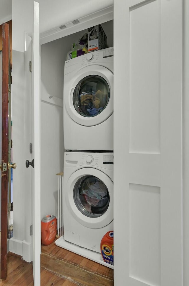 laundry room featuring stacked washer / drying machine and wood-type flooring