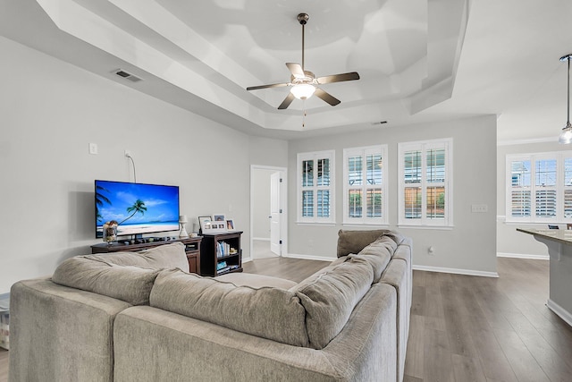 living area featuring visible vents, dark wood-type flooring, a ceiling fan, a tray ceiling, and baseboards