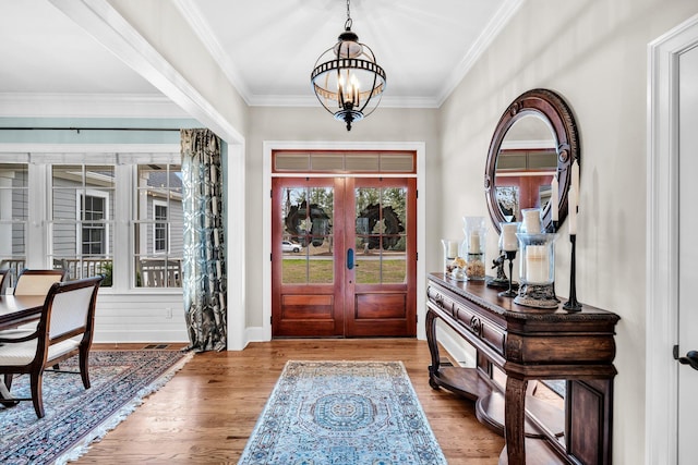 entrance foyer with a chandelier, french doors, wood finished floors, and crown molding