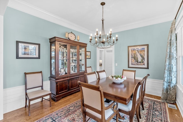 dining space with a wainscoted wall, visible vents, ornamental molding, light wood-type flooring, and an inviting chandelier