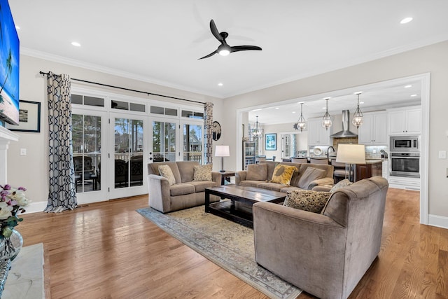 living area featuring recessed lighting, ornamental molding, wood finished floors, baseboards, and ceiling fan with notable chandelier