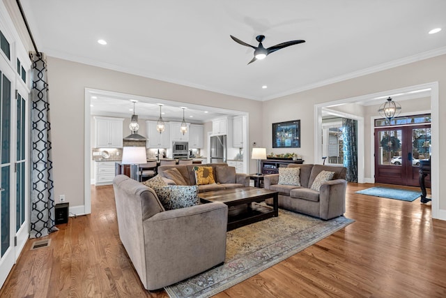 living area with recessed lighting, wood finished floors, visible vents, baseboards, and crown molding