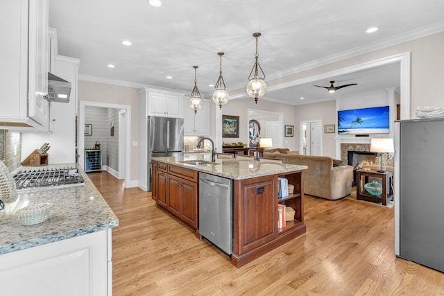 kitchen with light wood-style flooring, appliances with stainless steel finishes, a lit fireplace, white cabinetry, and a sink