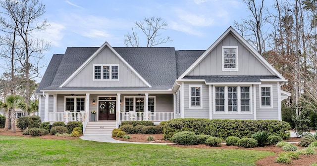 view of front of home with a ceiling fan, a porch, roof with shingles, a front lawn, and board and batten siding