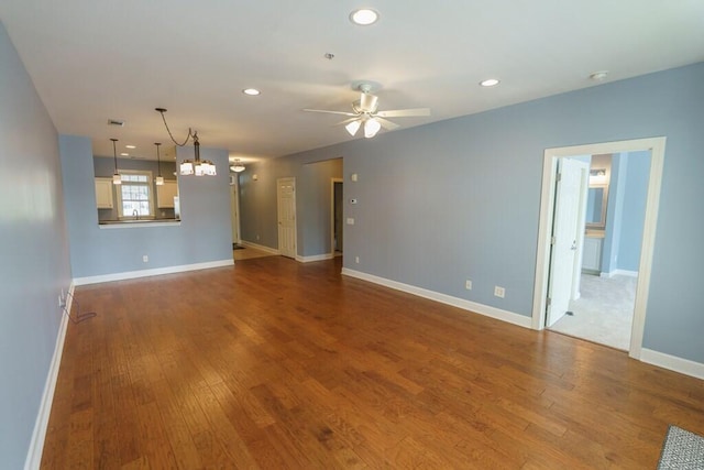 unfurnished living room with recessed lighting, ceiling fan with notable chandelier, baseboards, and wood finished floors