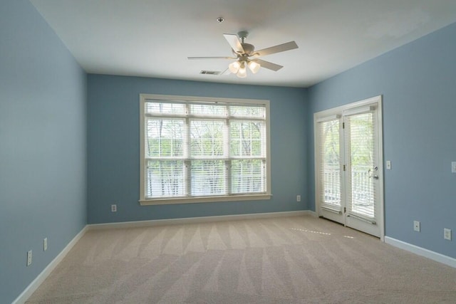 carpeted spare room with a healthy amount of sunlight, baseboards, a ceiling fan, and visible vents