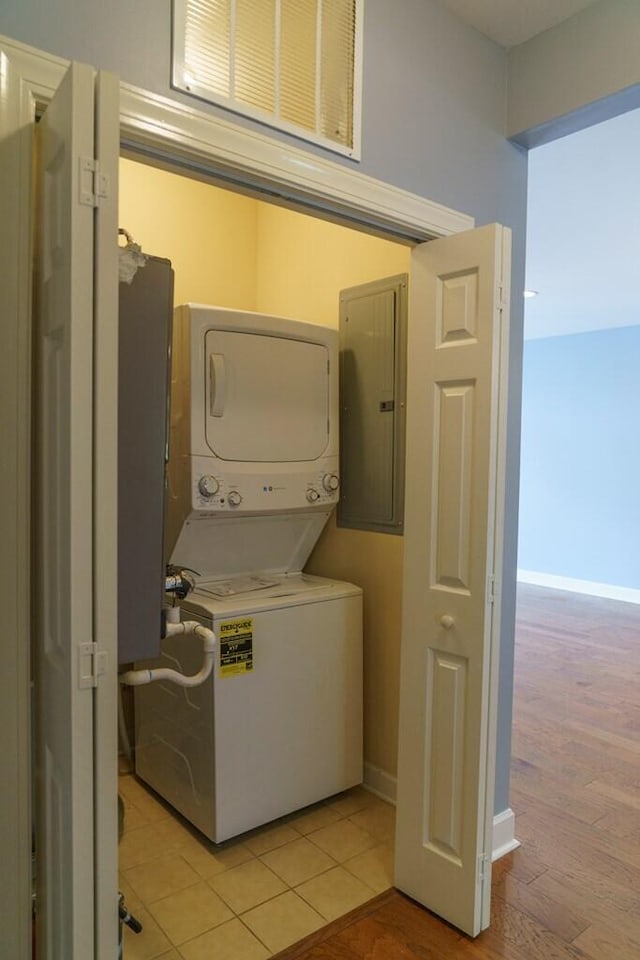 laundry room with baseboards, stacked washer / dryer, laundry area, and electric panel