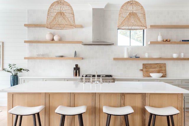 kitchen with wall chimney range hood, a center island with sink, a breakfast bar, decorative backsplash, and sink