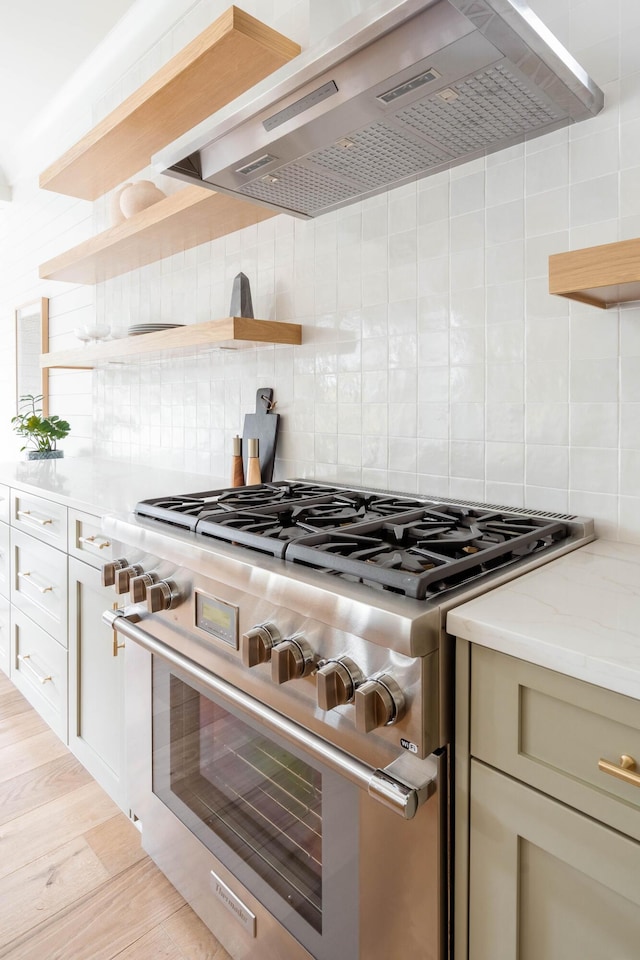 kitchen featuring wall chimney exhaust hood, light hardwood / wood-style floors, backsplash, high end stainless steel range oven, and light stone counters