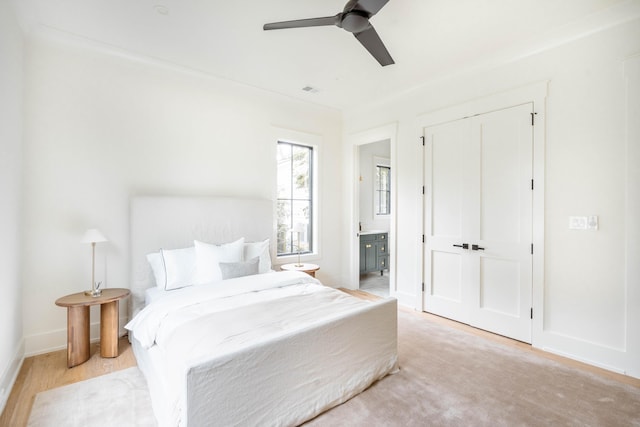 bedroom featuring ceiling fan, ensuite bathroom, a closet, and light hardwood / wood-style flooring