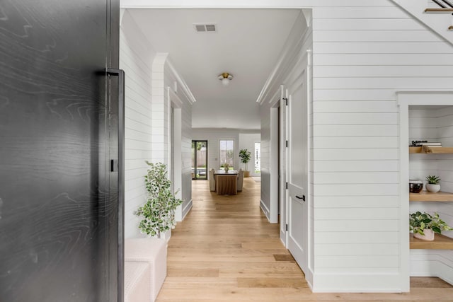 hall with crown molding, light hardwood / wood-style floors, and wooden walls