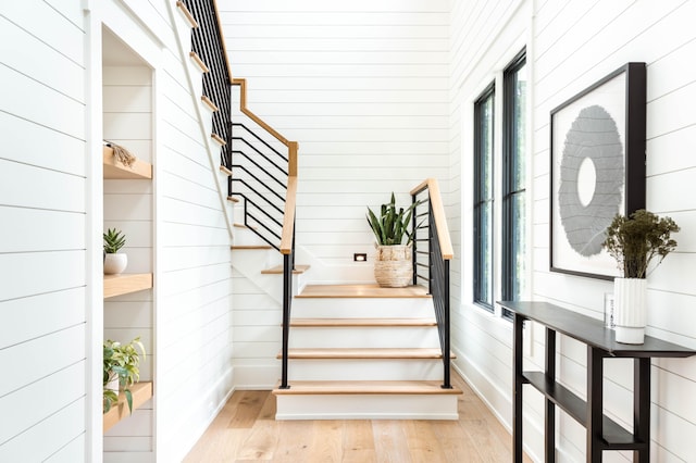 stairs with wood walls, a healthy amount of sunlight, and hardwood / wood-style floors