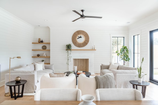 living room with ceiling fan, light hardwood / wood-style flooring, wood walls, and a premium fireplace