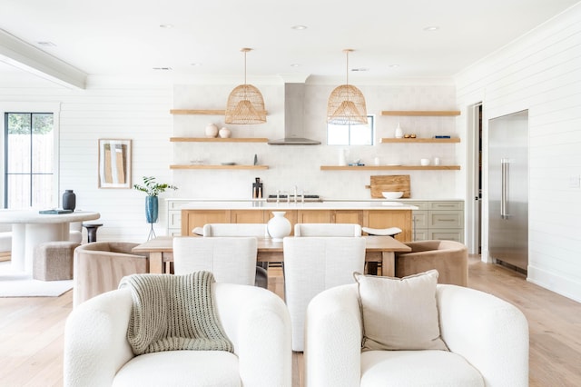 kitchen with decorative light fixtures, light hardwood / wood-style floors, stainless steel built in refrigerator, and wall chimney range hood