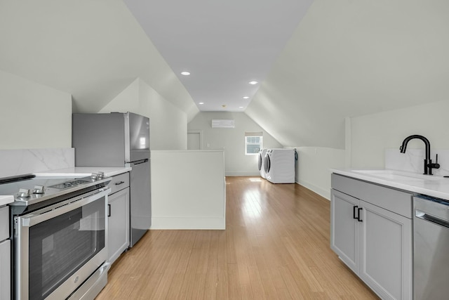 kitchen with vaulted ceiling, light wood-style flooring, appliances with stainless steel finishes, washer / clothes dryer, and a sink