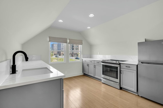 kitchen with gray cabinets, a sink, stainless steel appliances, vaulted ceiling, and light wood-type flooring