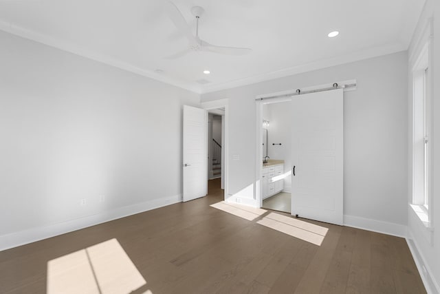 unfurnished bedroom featuring ensuite bathroom, dark hardwood / wood-style flooring, ornamental molding, ceiling fan, and a barn door