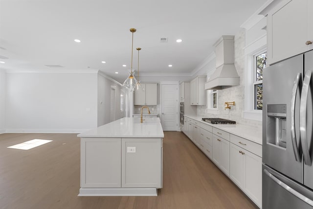 kitchen featuring crown molding, stainless steel appliances, custom range hood, an island with sink, and decorative light fixtures