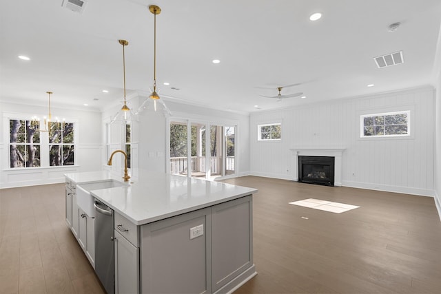 kitchen with dark hardwood / wood-style floors, sink, hanging light fixtures, a kitchen island with sink, and light stone countertops