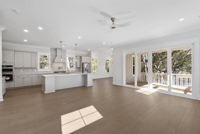 kitchen with premium range hood, appliances with stainless steel finishes, backsplash, hanging light fixtures, and a kitchen island with sink