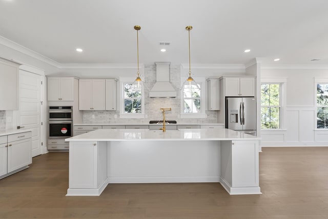 kitchen featuring white cabinetry, a center island with sink, custom range hood, pendant lighting, and stainless steel appliances