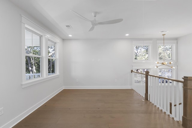 empty room featuring a healthy amount of sunlight, dark hardwood / wood-style floors, and ceiling fan with notable chandelier