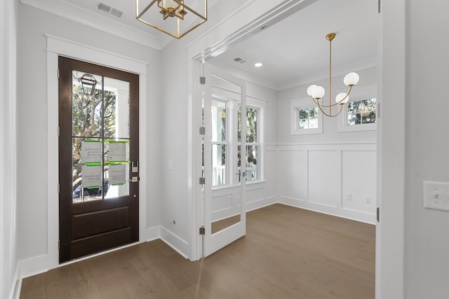 foyer entrance with crown molding, plenty of natural light, dark hardwood / wood-style floors, and a chandelier