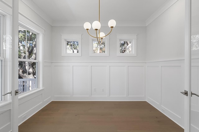 unfurnished dining area with dark wood-type flooring, ornamental molding, and a chandelier