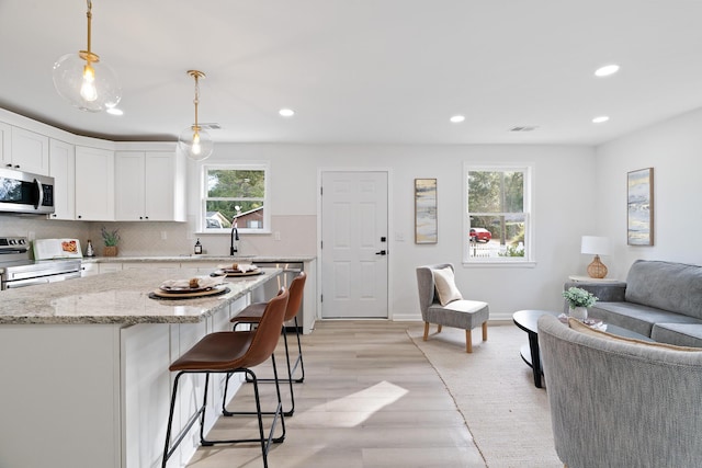 kitchen featuring stainless steel appliances, decorative light fixtures, white cabinetry, a kitchen island, and plenty of natural light