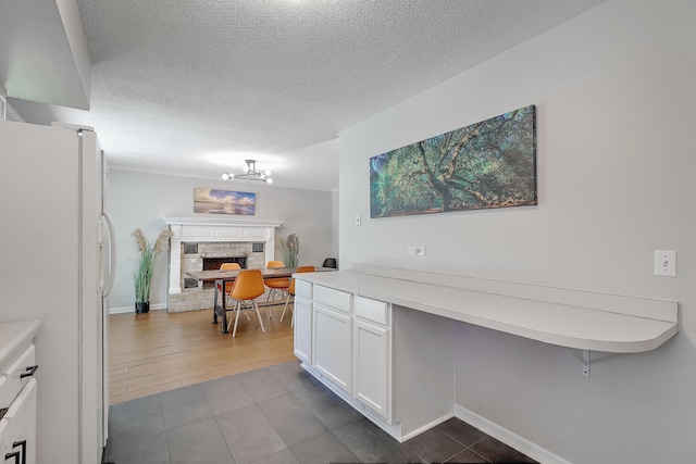 kitchen featuring white fridge, white cabinets, a textured ceiling, and a stone fireplace