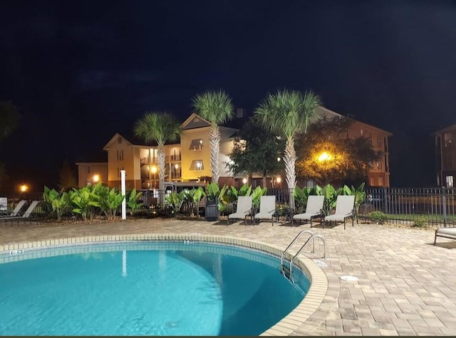 pool at night with a community pool, fence, and a patio