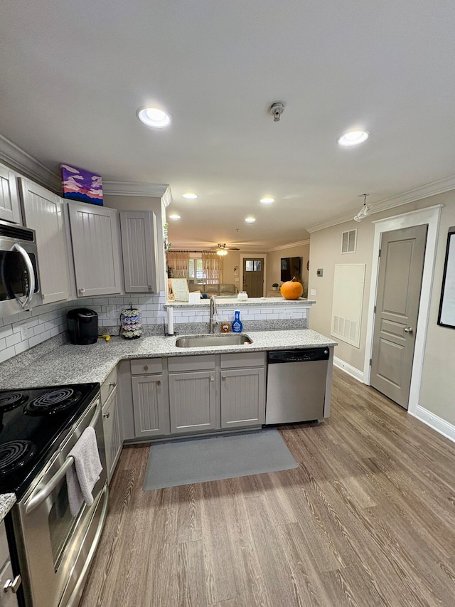 kitchen featuring kitchen peninsula, appliances with stainless steel finishes, hardwood / wood-style flooring, gray cabinets, and sink