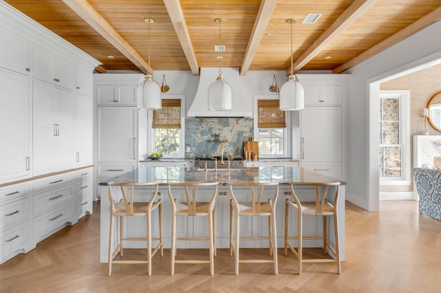 kitchen with pendant lighting, a breakfast bar, white cabinets, and a center island with sink