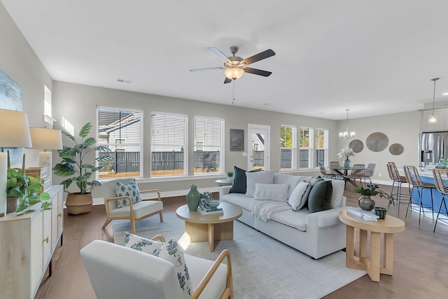 living room featuring ceiling fan with notable chandelier and light hardwood / wood-style flooring