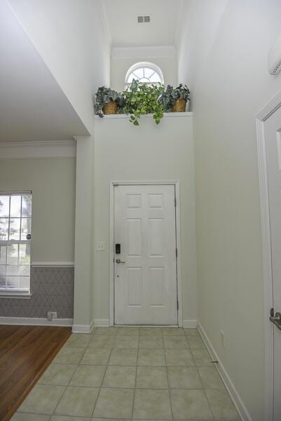 foyer with a high ceiling, light tile patterned floors, and crown molding