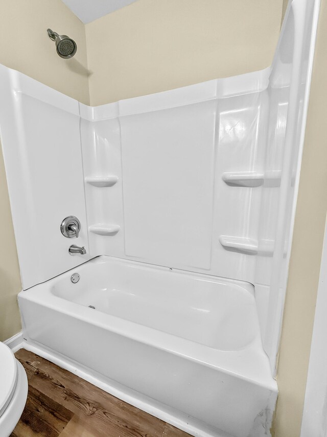 bathroom featuring wood-type flooring, toilet, and bathtub / shower combination