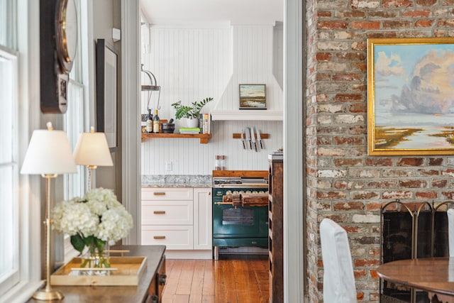 bar featuring dark wood-type flooring, light stone counters, brick wall, white cabinets, and high end stove