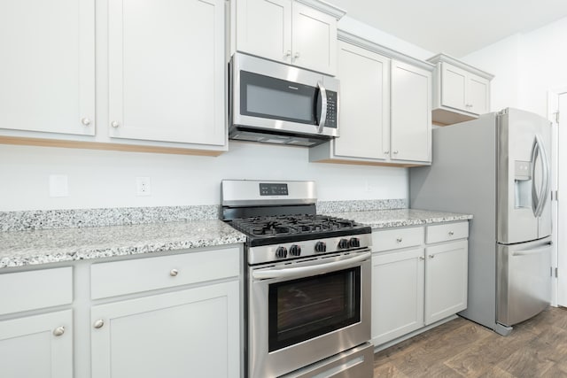 kitchen with white cabinetry, stainless steel appliances, light stone counters, and dark hardwood / wood-style flooring