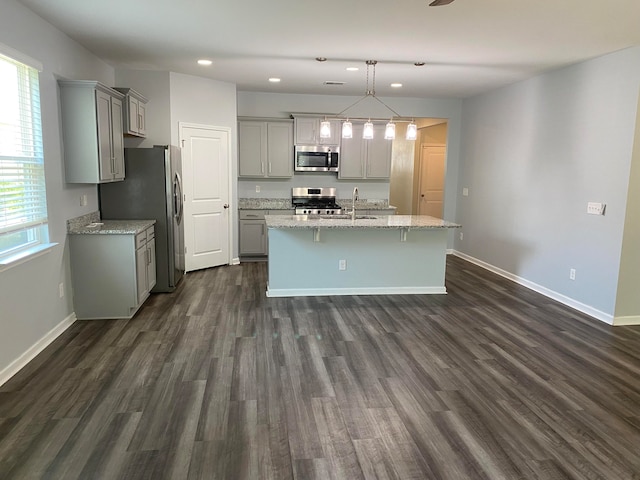 kitchen featuring light stone counters, dark wood-type flooring, pendant lighting, gray cabinets, and stainless steel appliances