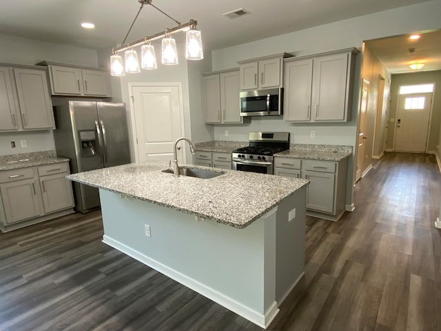 kitchen featuring light stone counters, an island with sink, appliances with stainless steel finishes, dark hardwood / wood-style flooring, and sink