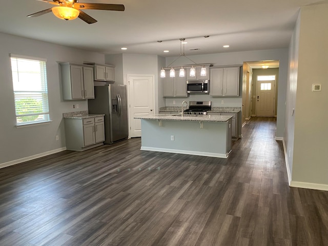 kitchen with a center island with sink, dark hardwood / wood-style flooring, appliances with stainless steel finishes, gray cabinets, and decorative light fixtures