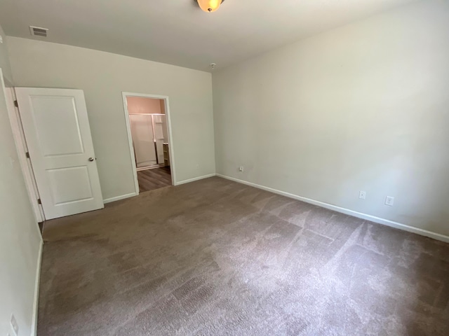 unfurnished bedroom featuring a spacious closet, dark carpet, and a closet